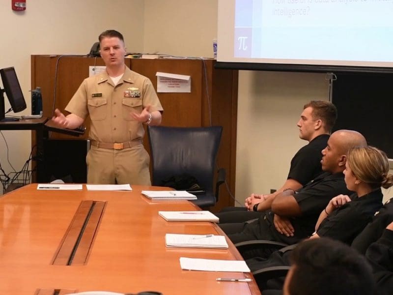 LCDR Joseph M. Hatfield speaks to a roomful of people