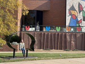 Ulrich Museum Registrar Jo Cox sits within the new Hank Willis Thomas sculpture, "Ernest and Ruth," installed yesterday in front of the museum.