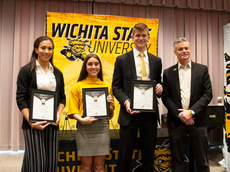 The three winners stand with President Muma holding their certificates behind big WSU banner.