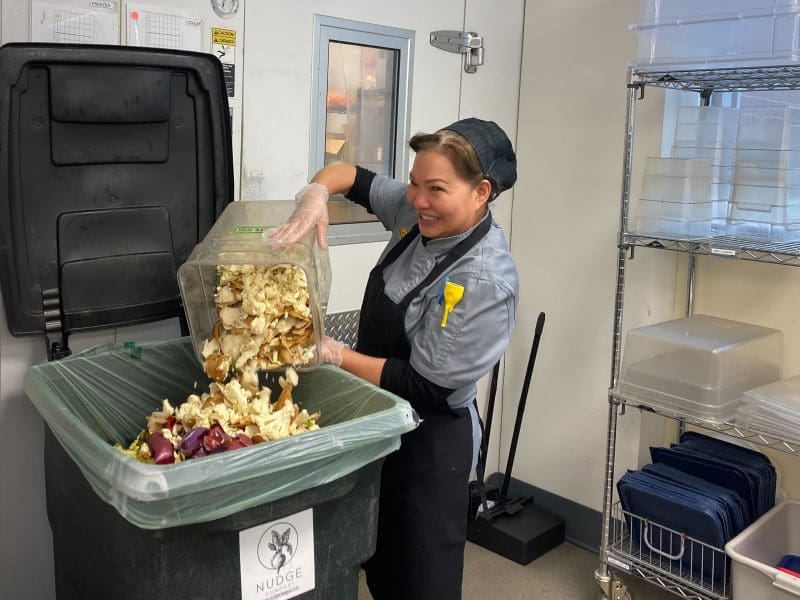 Picture of Khristin Nguyen, a member of the Chartwells kitchen crew, dumps food waste into a composting bin in Shocker Hall