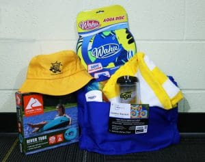 The picture includes an SCA bucket hat and tumbler, beach towel, outdoor blanket, water frisbee, sunscreen, and a river tube.