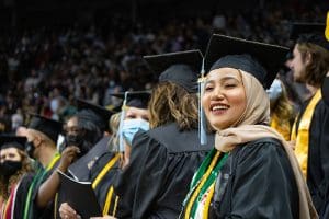 Image of three graduates with a large group of graduates behind them at Hughes Metro Complex.