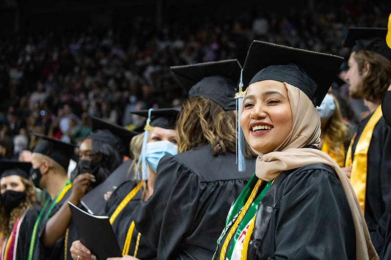 Image of three graduates with a large group of graduates behind them at Hughes Metro Complex.
