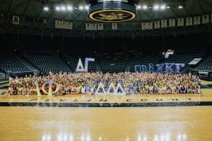 A large group photo of all 5 chapters celebrating on Bid Day. Each chapter is holding up signs in the shape of their chapters' Greek letters.