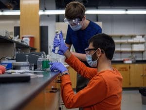 Chemistry students study over a lab table.