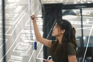A photo of a person writing on a glass panel.