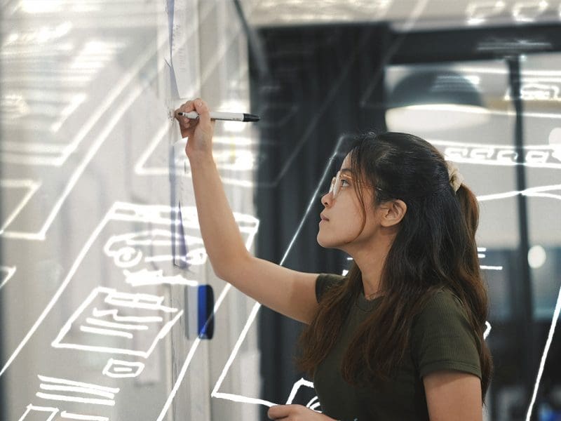 A photo of a person writing on a glass panel.