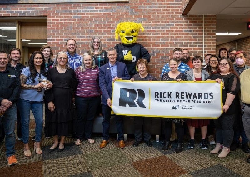 Photo of President Rick Muma with members of the Media Resources Center and WuShock holding up a sign that says "Rick Rewards | The Office of the President."