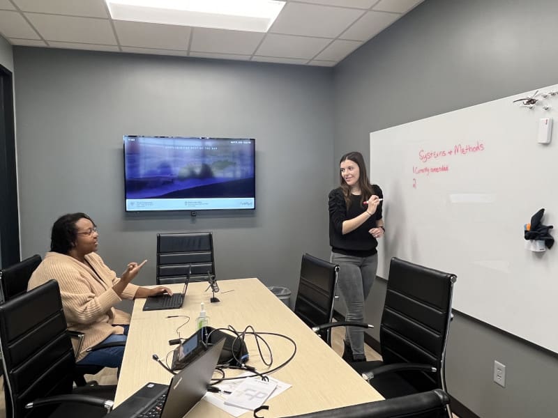 Photo of two students in the Office of Tech Transfer and Commercialization working through a problem on a whiteboard.