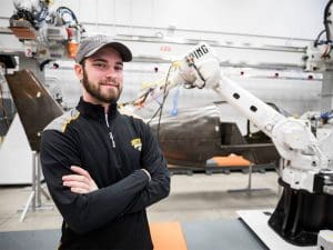 A student stands in front of a robotics arm in the Applied Engineering Department