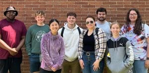 Wichita State students in the program post in front of a brick wall