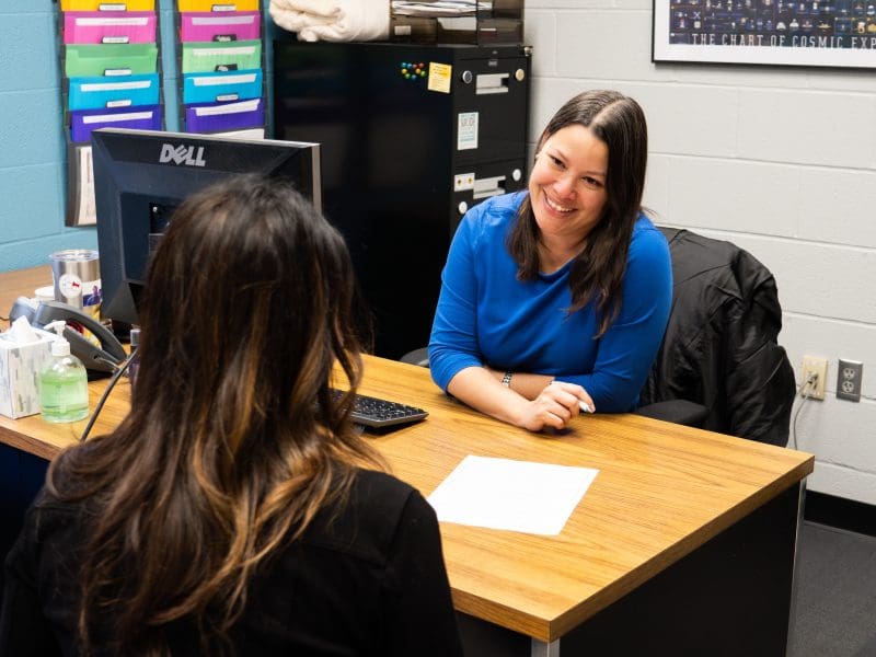 An academic advisor sits at a desk facing a student.