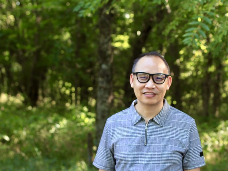 Hong Tien Vu stands in front of a wooded area