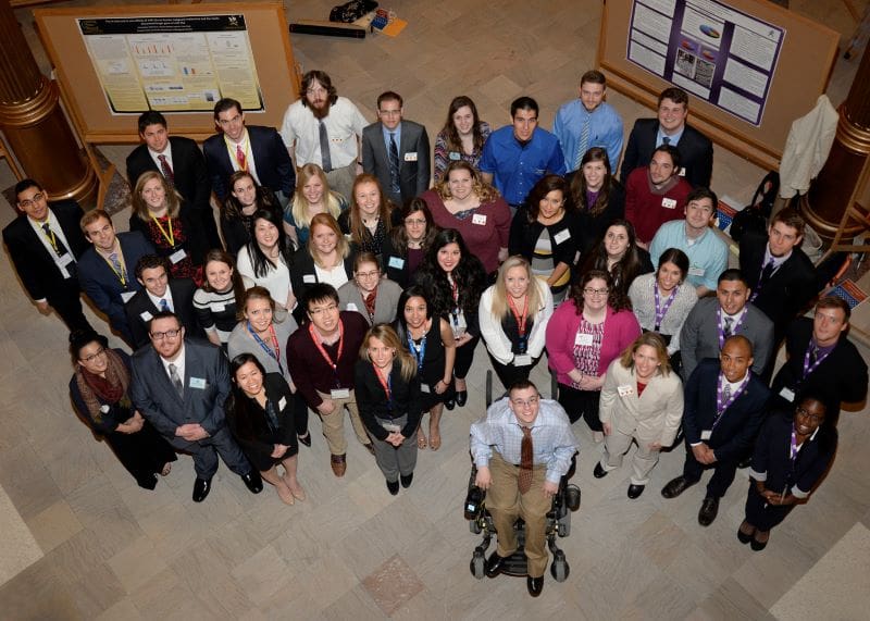 A group of 40 student researchers standing in the capitol building rotunda and looking up at the photographer