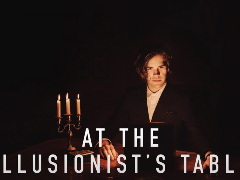 "At the Illusionist's Table" Photo shows a young man in candlelight at a table