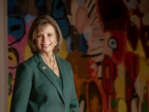 Elizabeth King poses in front of colorful artwork wearing a green blazer