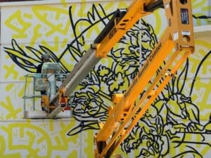 Artist GLeo paints a mural on the walls of Duerksen Amphitheatre from a mechanical lift.