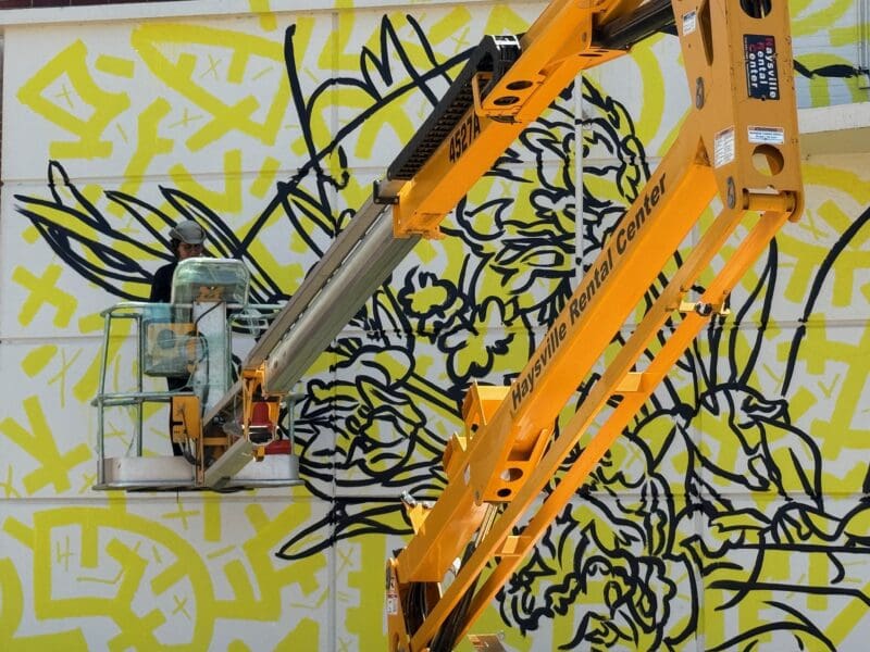 Artist GLeo paints a mural on the walls of Duerksen Amphitheatre from a mechanical lift.