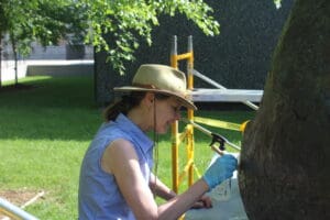 A woman in a hat cleans a sculpture with a dry paintbrush.