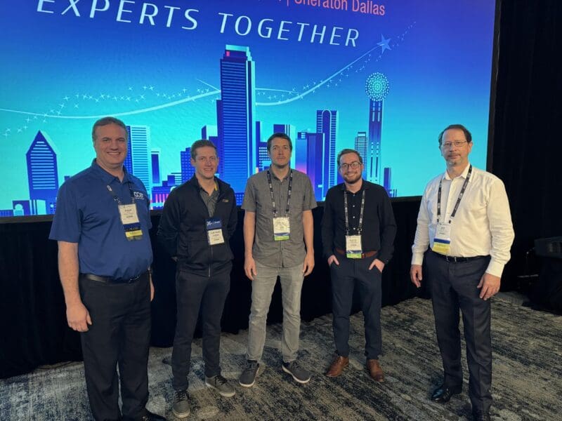 Roger Joyal (Dassault Systèmes), Jeremy Sitz (WSU-NIAR), Samuel Eshelman (Stanley Black and Decker), Hunter Robertson (WSU-NIAR) and Eric Neuville (Dassault Systèmes) pose in front of a blue digital backdrop depicting the Dallas skyline.