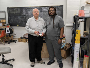Dr. Nick Solomey and Tyler Nolan show off the prototype radiation detector they are studying bathed in UV light