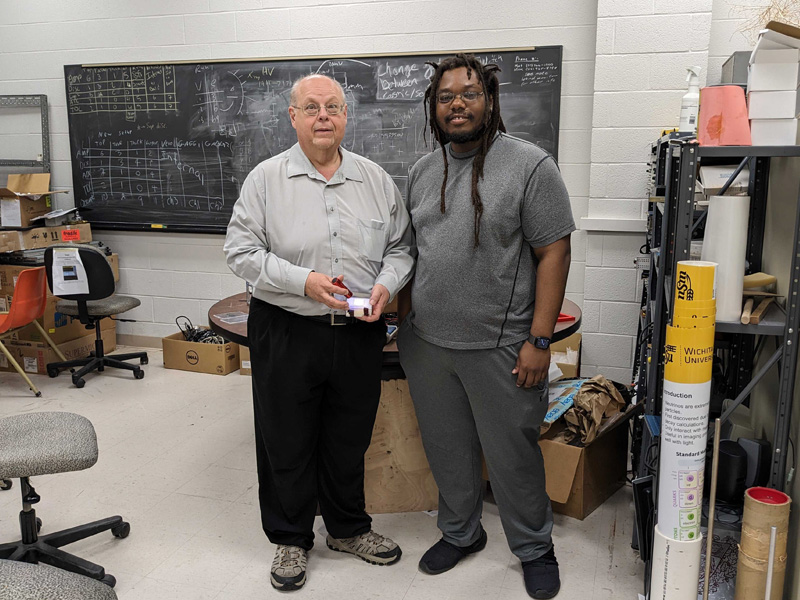 Dr. Nick Solomey and Tyler Nolan show off the prototype radiation detector they are studying bathed in UV light