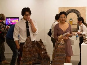 Man and woman looking at clay artwork. More people in background talking and looking at artwork.