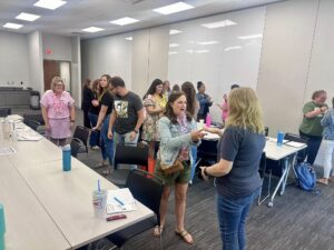 Attendees at the SELebration Conference engage in an interactive activity during a breakout session. Pairs of participants are standing face-to-face, talking and laughing in a bright, modern classroom setting.
