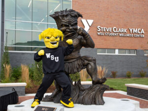 WuShock poses with his sculpture in front of the Steve Clark YMCA on Wichita State's campus