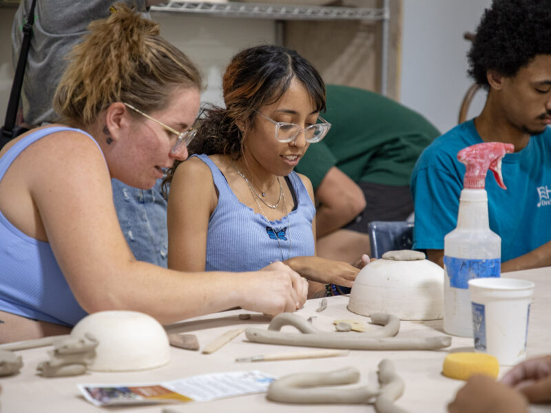 Three young people create ceramic bowls at a table.