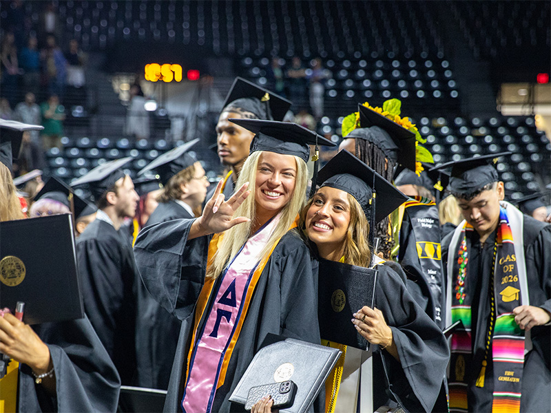 Graduates at commencement in their gowns pose for the camera in Charles Koch Arena