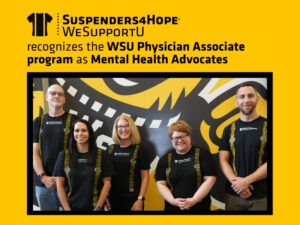 Members of the physician associate program pose of front of a mural of WuShock. The members are wearing black T-shirts with yellow suspenders printed on them and "Suspenders4Hope" on the front. A yellow border surrounds the photo and text at the top reads "Suspenders4Hope, WeSupportU, recognized the WSU Physician Associate Program as Mental Health Advocates"