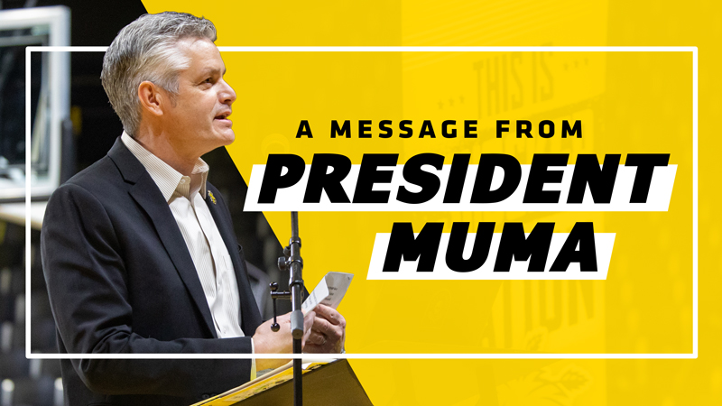 The text "A message from President Muma" on a yellow background that cuts the graphic in half. On the other half is Rick Muma speaking to a crown from a podium.