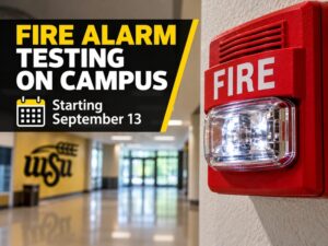 WSU campus hallway with a red fire alarm and strobe light, promoting annual fire alarm testing beginning September 13