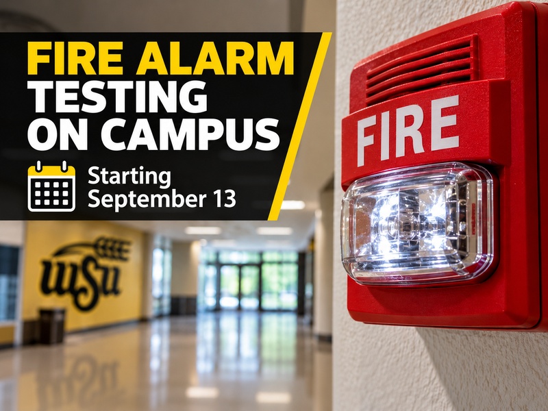 WSU campus hallway with a red fire alarm and strobe light, promoting annual fire alarm testing beginning September 13