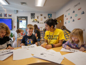 A Wichita State student sits with school children helping them with school projects.
