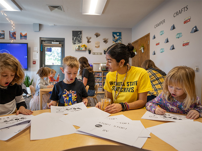 A Wichita State student sits with school children helping them with school projects.